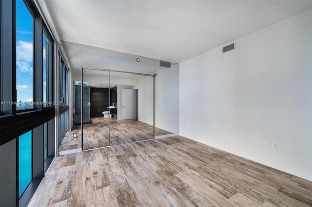 unfurnished bedroom with baseboards, visible vents, wood finished floors, and a closet