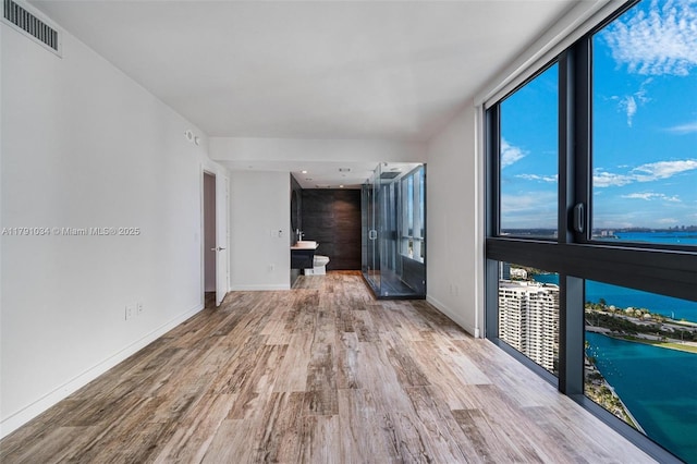 spare room featuring wood finished floors, visible vents, a water view, and baseboards