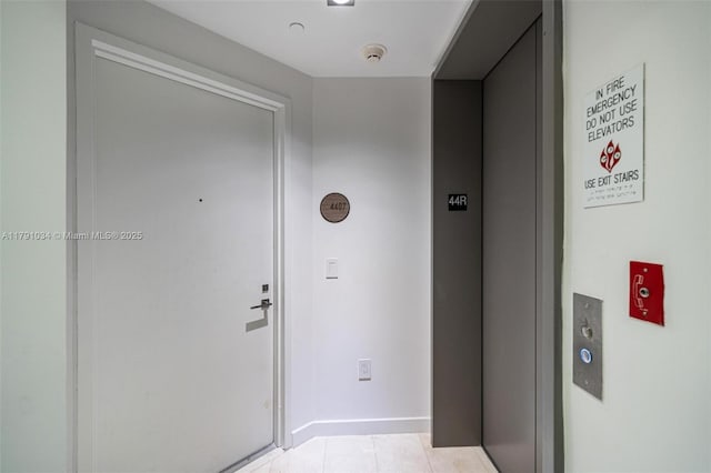 corridor featuring light tile patterned floors, elevator, and baseboards