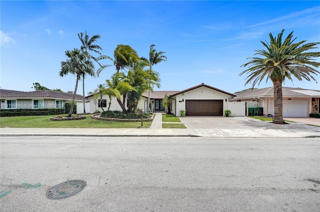 ranch-style house with driveway, stucco siding, a front yard, fence, and a garage