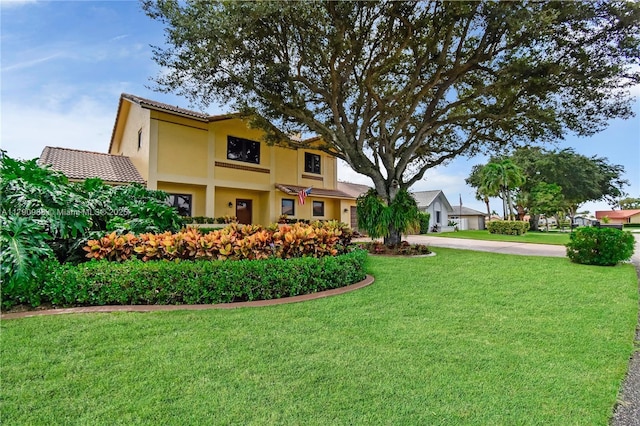 view of front of house featuring stucco siding, a tile roof, and a front yard