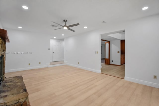 unfurnished living room with a ceiling fan, light wood-type flooring, baseboards, a fireplace with raised hearth, and recessed lighting