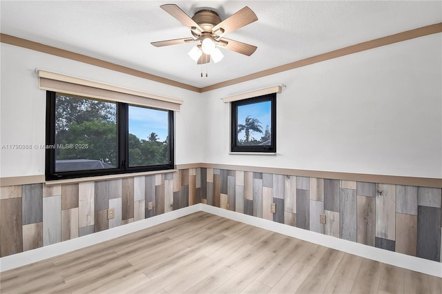spare room with a ceiling fan, wainscoting, wood finished floors, and a healthy amount of sunlight