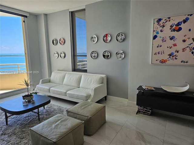 living room featuring marble finish floor, a water view, and baseboards