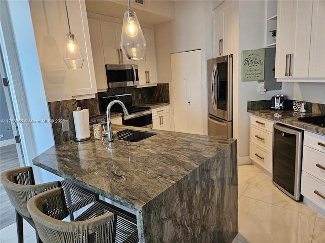 kitchen with a sink, wine cooler, dark stone countertops, a peninsula, and appliances with stainless steel finishes
