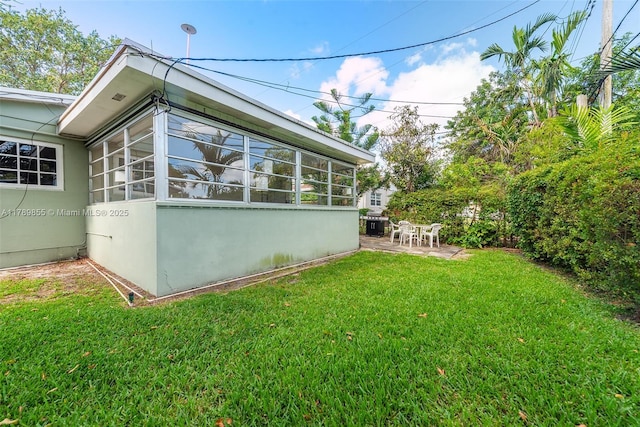 view of property exterior featuring a sunroom, a lawn, stucco siding, and a patio