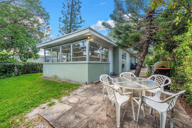 back of property featuring outdoor dining area, stucco siding, a sunroom, a patio area, and a yard