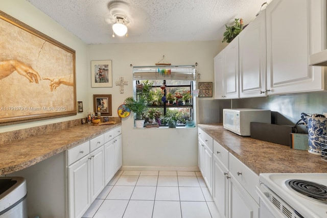 kitchen featuring white microwave, light tile patterned floors, white cabinets, baseboards, and a textured ceiling