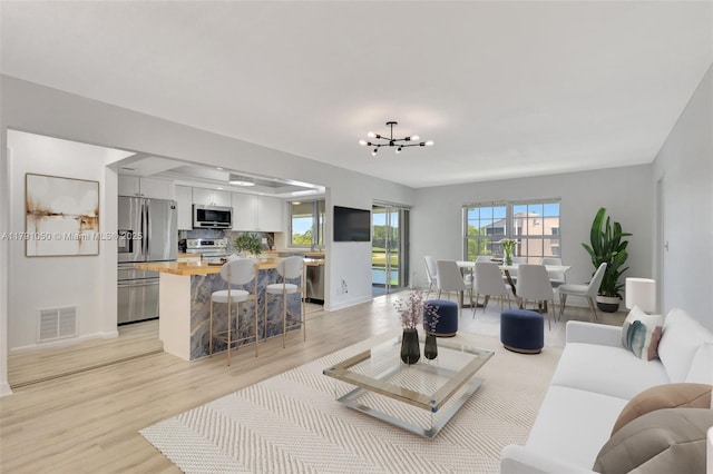 living area featuring visible vents, baseboards, a chandelier, and light wood-type flooring
