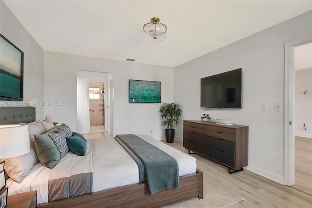 bedroom with baseboards, light wood-type flooring, and ensuite bath