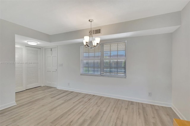 unfurnished room with baseboards, an inviting chandelier, light wood-style flooring, and visible vents