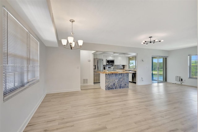 unfurnished living room featuring baseboards, a notable chandelier, light wood finished floors, and visible vents