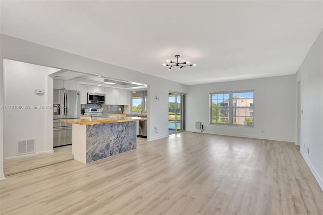 unfurnished living room with visible vents, an inviting chandelier, baseboards, a sink, and light wood finished floors