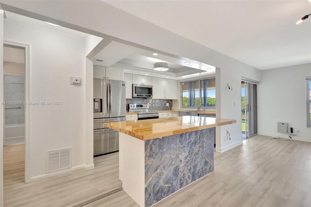 kitchen featuring a sink, a raised ceiling, wooden counters, stainless steel appliances, and visible vents