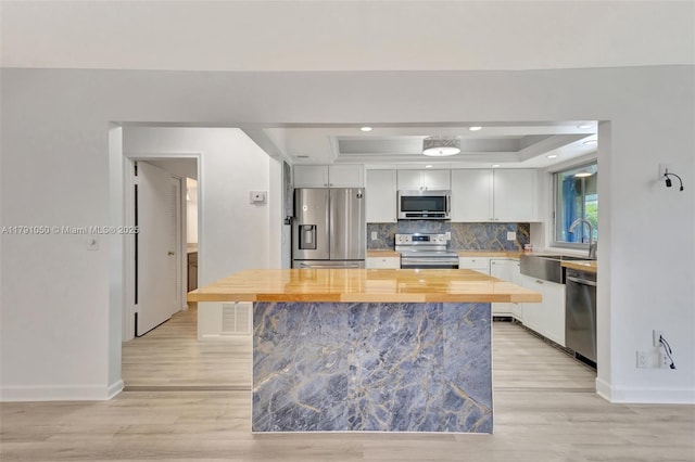 kitchen with a sink, a raised ceiling, butcher block counters, light wood-style floors, and stainless steel appliances