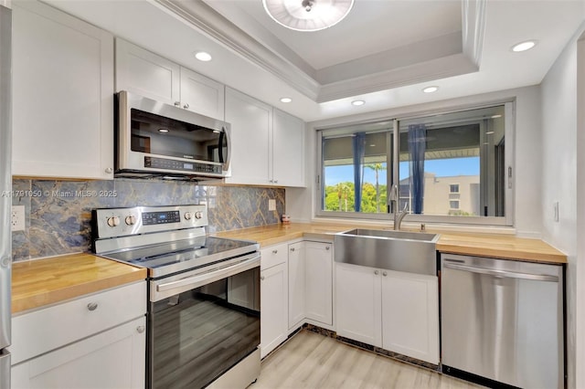 kitchen with decorative backsplash, appliances with stainless steel finishes, a sink, light wood-style floors, and wood counters