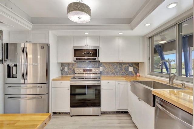 kitchen featuring wooden counters, a sink, a raised ceiling, light wood finished floors, and stainless steel appliances