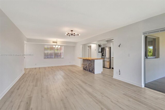 unfurnished living room with baseboards, a chandelier, visible vents, and light wood-type flooring