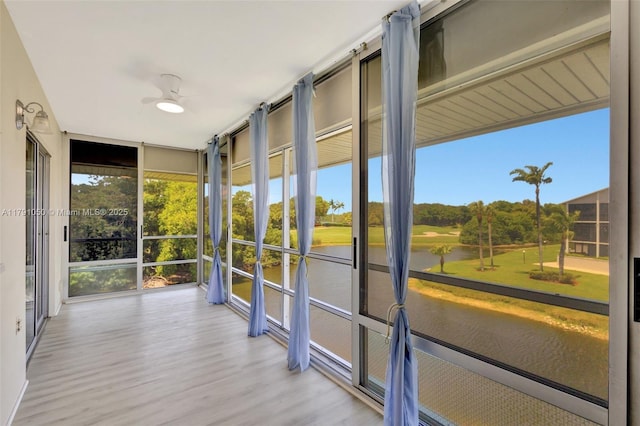 unfurnished sunroom with a water view, ceiling fan, a wall of windows, and wood finished floors