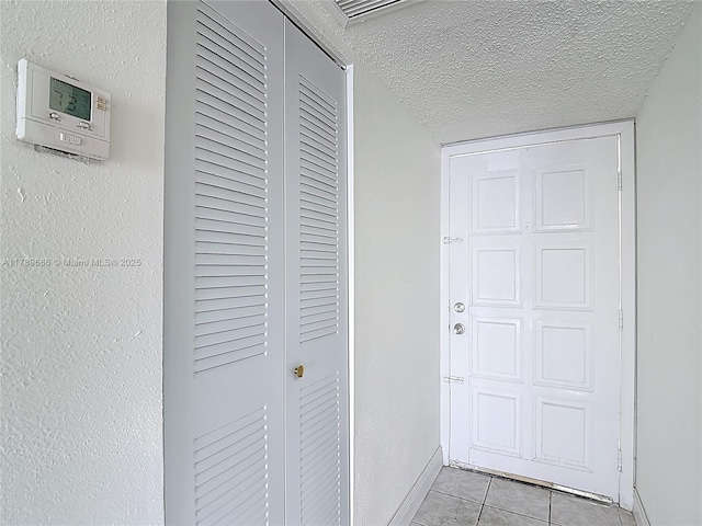 hall featuring light tile patterned floors, baseboards, and a textured ceiling