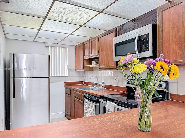 kitchen with stainless steel appliances, a sink, brown cabinets, a drop ceiling, and open shelves