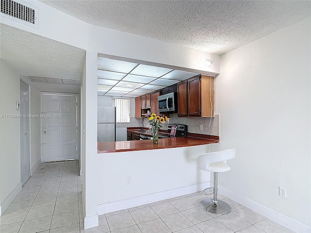 kitchen featuring stainless steel appliances, light tile patterned floors, dark countertops, a sink, and a textured ceiling