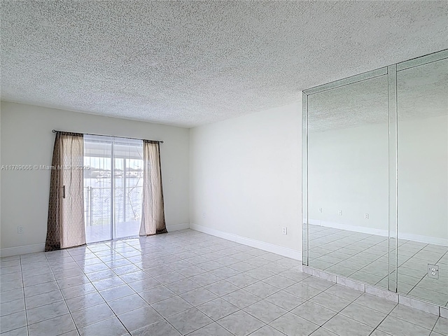 spare room with light tile patterned flooring, a textured ceiling, and baseboards