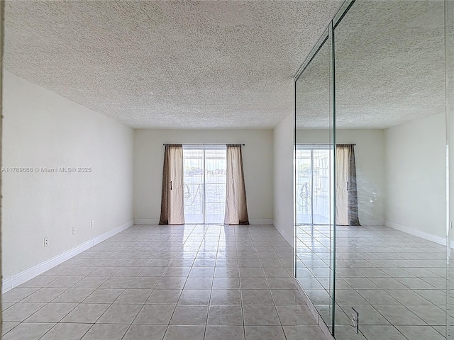 spare room featuring light tile patterned floors, a textured ceiling, and baseboards
