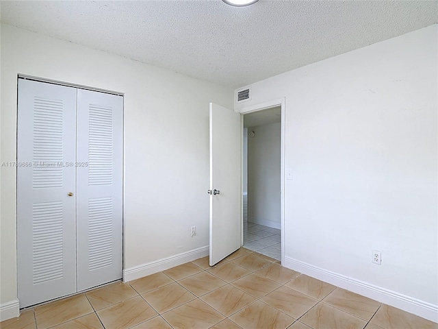 unfurnished bedroom featuring a closet, light tile patterned floors, a textured ceiling, and baseboards