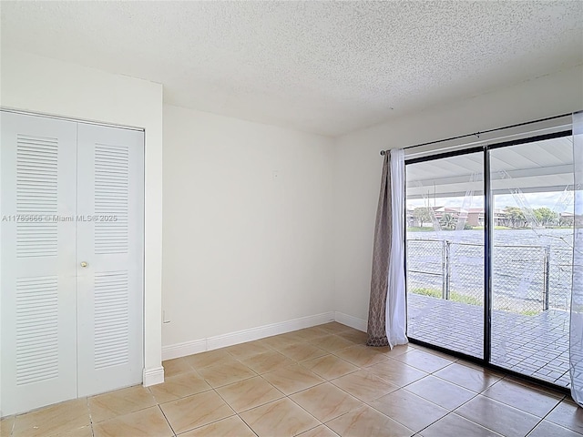 empty room with a textured ceiling, light tile patterned floors, and baseboards