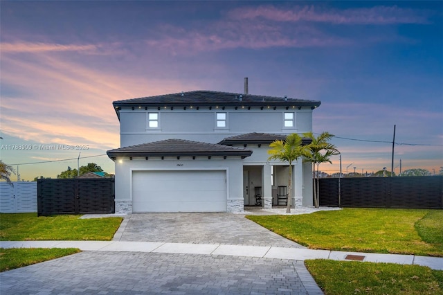 view of front of house featuring a front yard, stone siding, decorative driveway, stucco siding, and fence