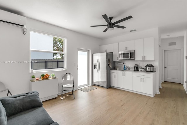 kitchen with a wall unit AC, visible vents, stainless steel appliances, light wood finished floors, and a ceiling fan