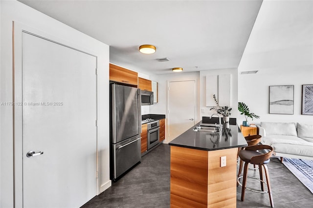 kitchen featuring a sink, appliances with stainless steel finishes, dark countertops, visible vents, and a kitchen bar