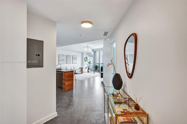 hallway with an inviting chandelier, visible vents, electric panel, and baseboards