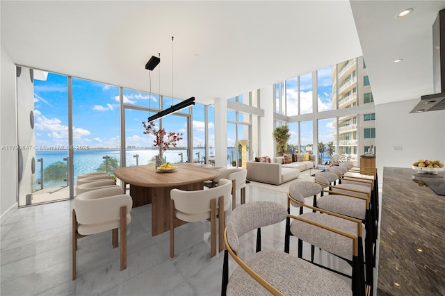 dining room with floor to ceiling windows, a water view, and a high ceiling