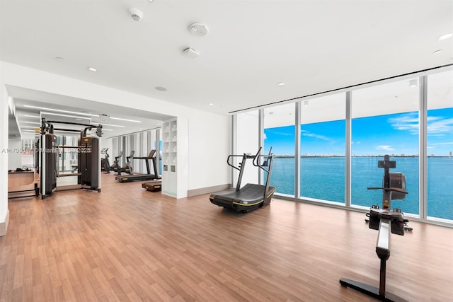 exercise room featuring wood finished floors, a wall of windows, and a water view