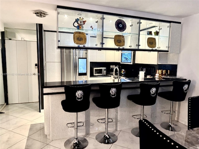 kitchen featuring appliances with stainless steel finishes, light tile patterned flooring, dark countertops, and a breakfast bar