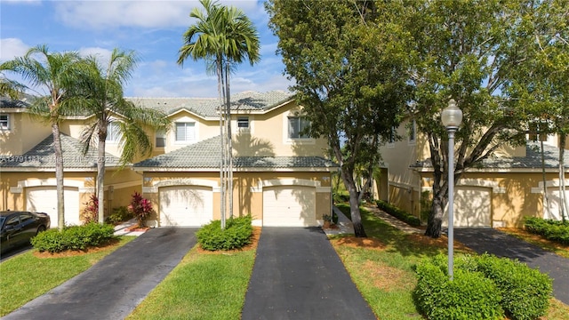 townhome / multi-family property with a tiled roof, an attached garage, stucco siding, and aphalt driveway