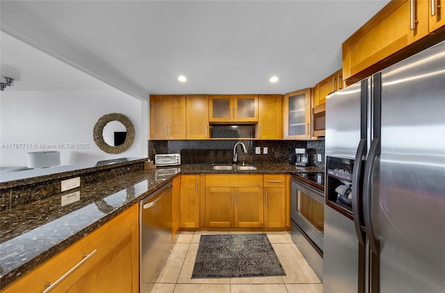 kitchen with dark stone countertops, light tile patterned floors, brown cabinets, a sink, and appliances with stainless steel finishes