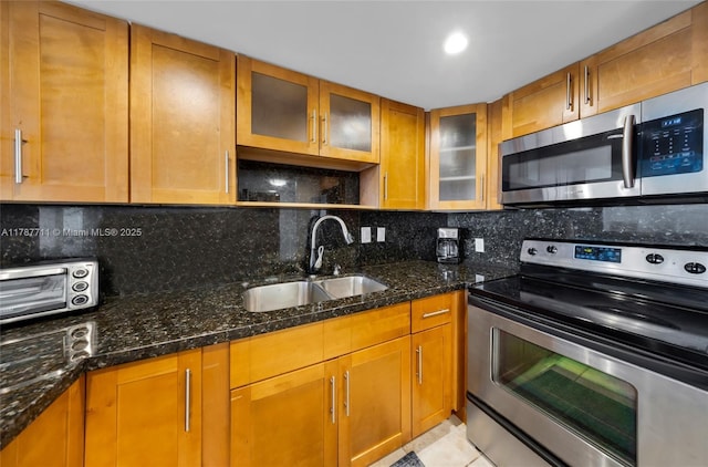 kitchen with brown cabinets, decorative backsplash, glass insert cabinets, a sink, and appliances with stainless steel finishes