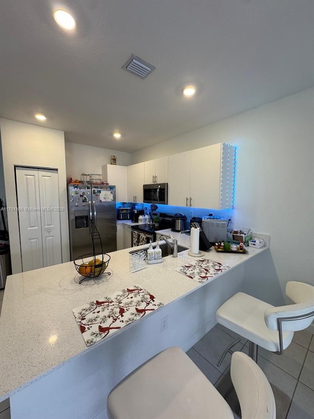 kitchen with a breakfast bar, visible vents, white cabinetry, a peninsula, and appliances with stainless steel finishes