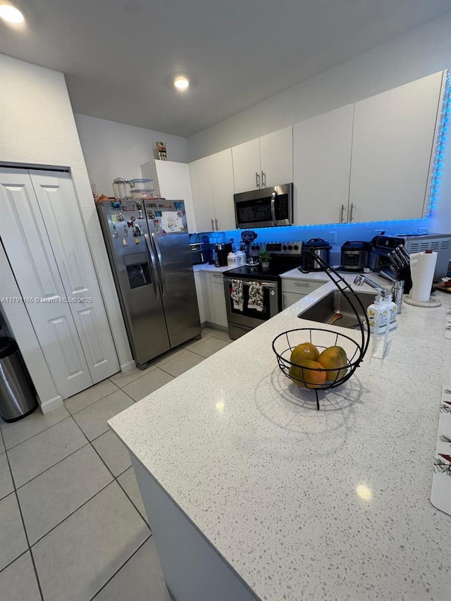 kitchen featuring light tile patterned floors, stainless steel appliances, white cabinets, a sink, and a peninsula