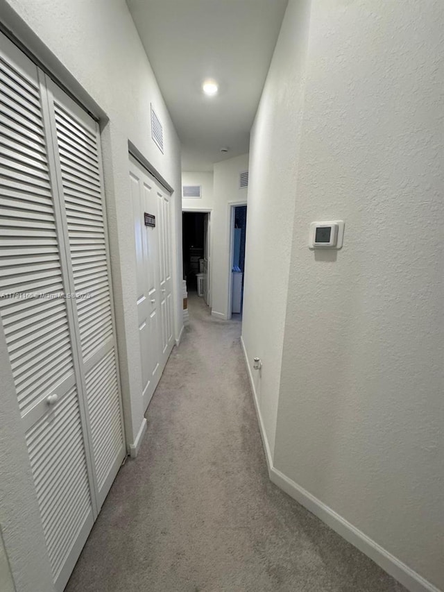 hall with visible vents, baseboards, a textured wall, and light carpet