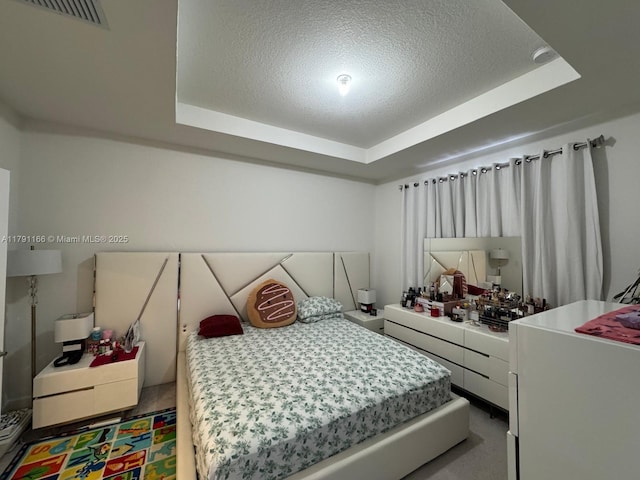 bedroom featuring a textured ceiling, visible vents, and a tray ceiling
