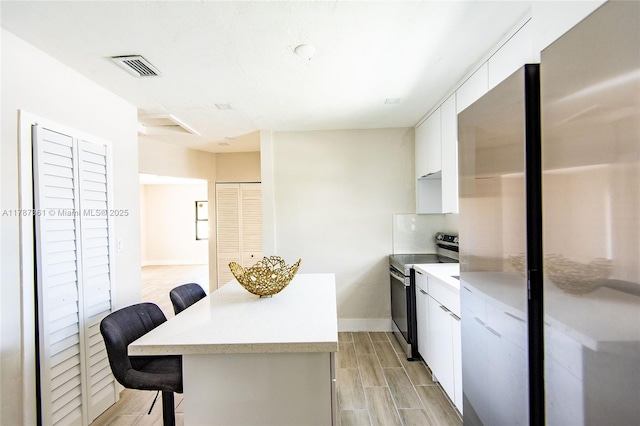 1710 E 6th Ave, Hialeah, FL 33010 - kitchen with appliances with stainless steel finishes, a kitchen bar, a kitchen island, light countertops, and white cabinets