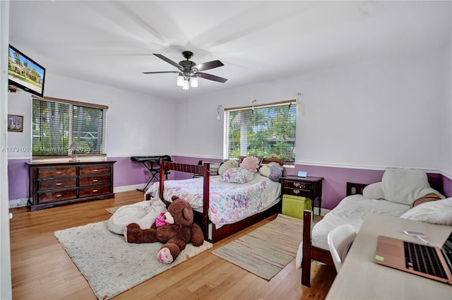 bedroom with a ceiling fan, multiple windows, wood finished floors, and baseboards