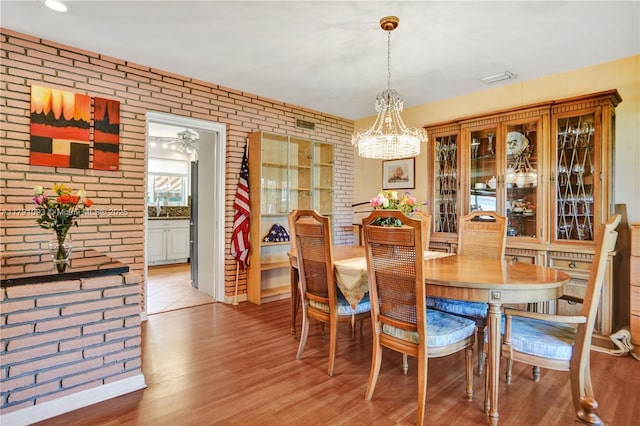 dining room featuring light wood finished floors, brick wall, and a notable chandelier