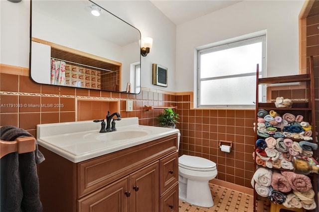 full bath featuring toilet, tile walls, tile patterned floors, vanity, and wainscoting
