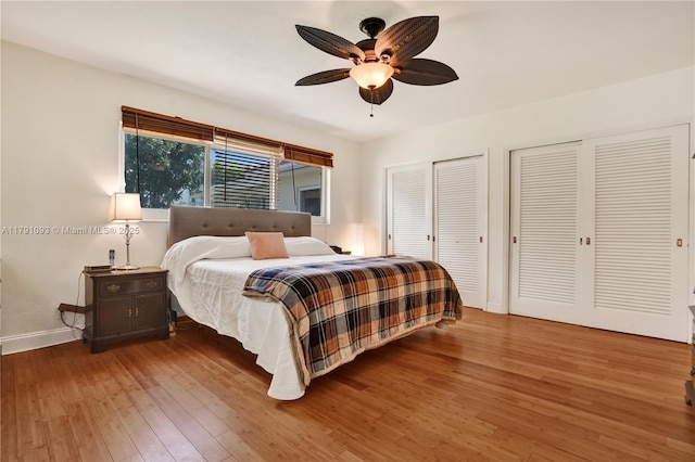 bedroom featuring hardwood / wood-style flooring, ceiling fan, multiple closets, and baseboards