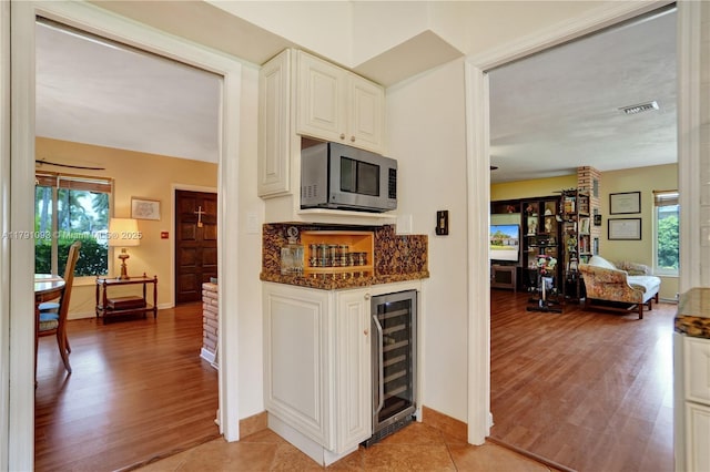 bar with stainless steel microwave, visible vents, light wood-style flooring, and beverage cooler
